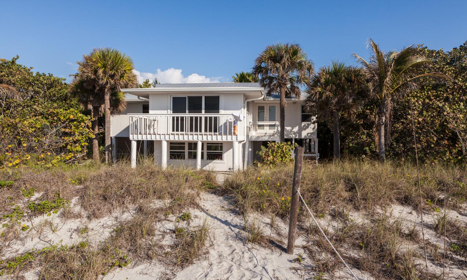 A white house behind dunes and palms